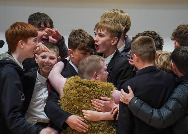 A group of school boys are hugging an Electric Umbrella member