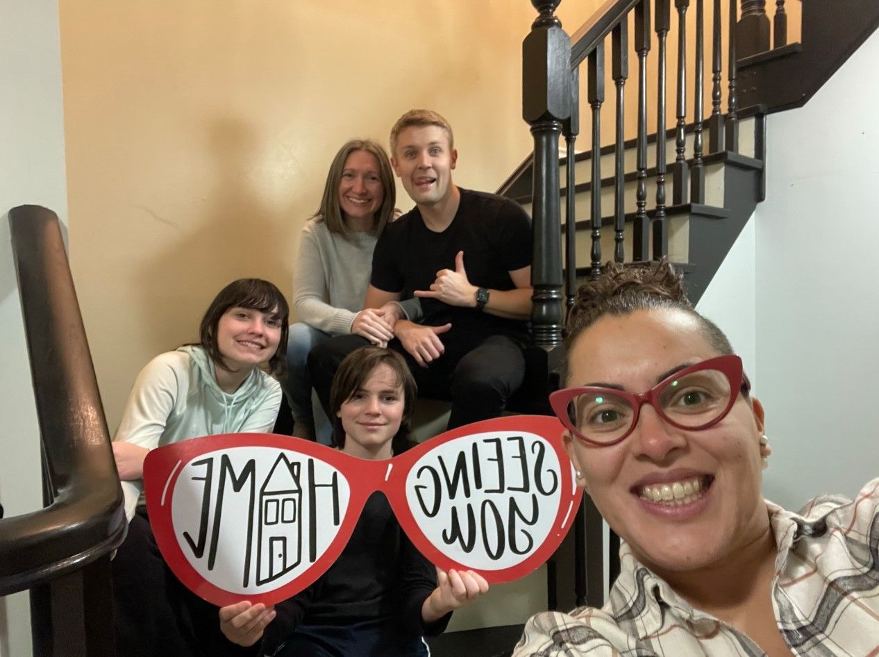 Group posing on stairs with red heart signs reading “I am” and “feel loved,” smiling at the camera.
