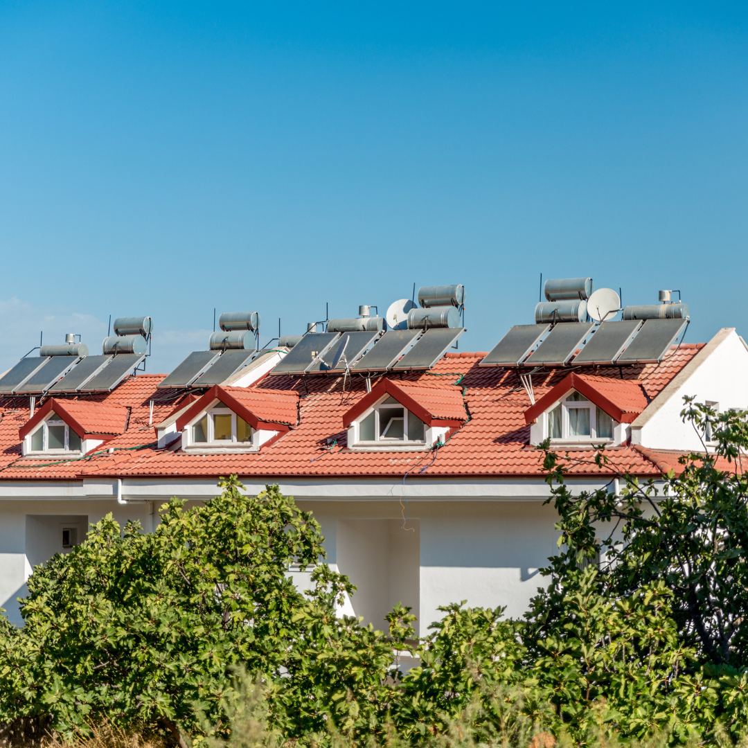 Red-roofed apartment building with rooftop solar water heaters under a clear blue sky