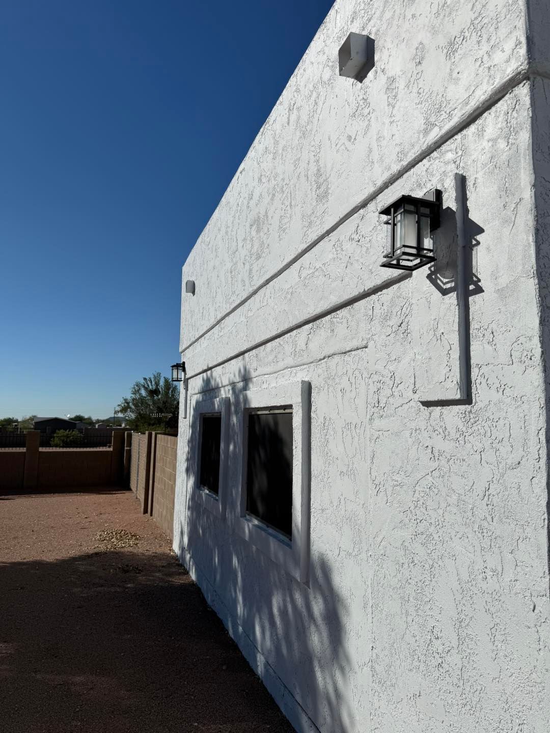 White stucco building exterior with black lamp and conduit against a blue sky.