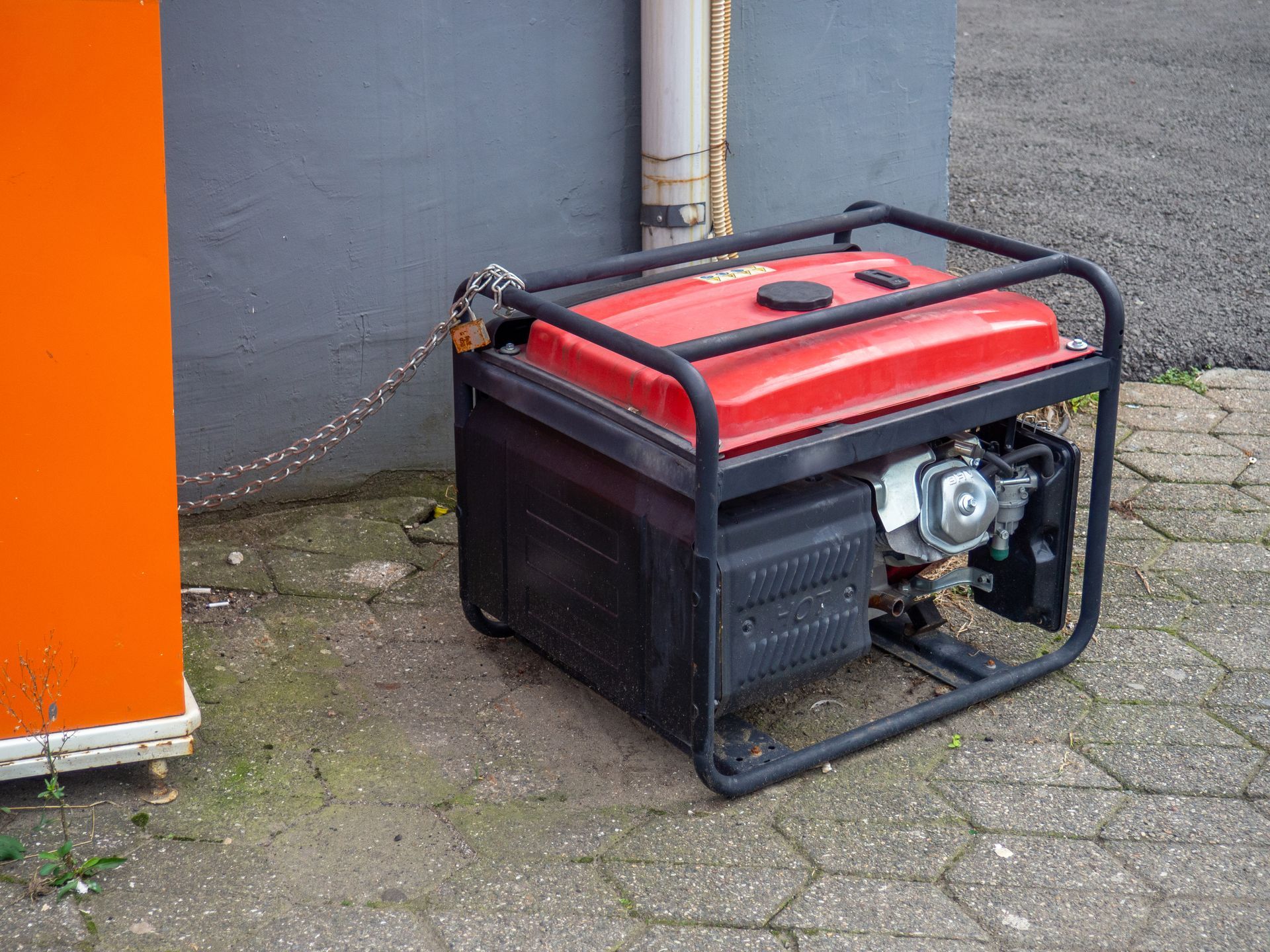 Red portable generator on a brick surface next to a gray wall and orange structure.