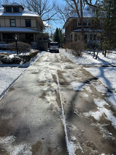 A car is driving down a snowy driveway next to a house.