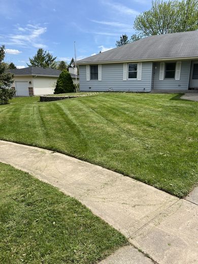 A house with a lush green lawn and a sidewalk in front of it.