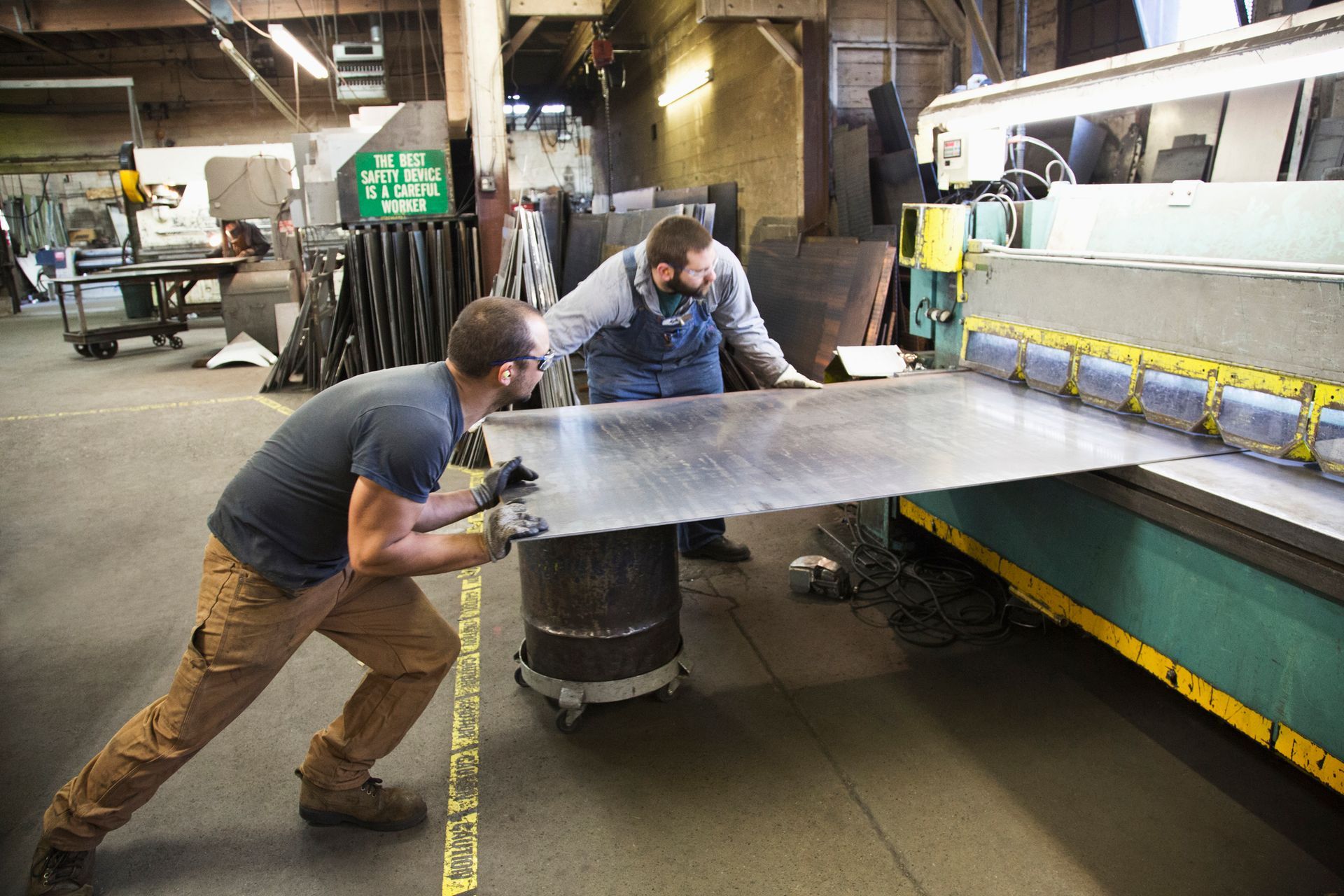 Two men working in a workshop, using a large machine to cut metal sheets.