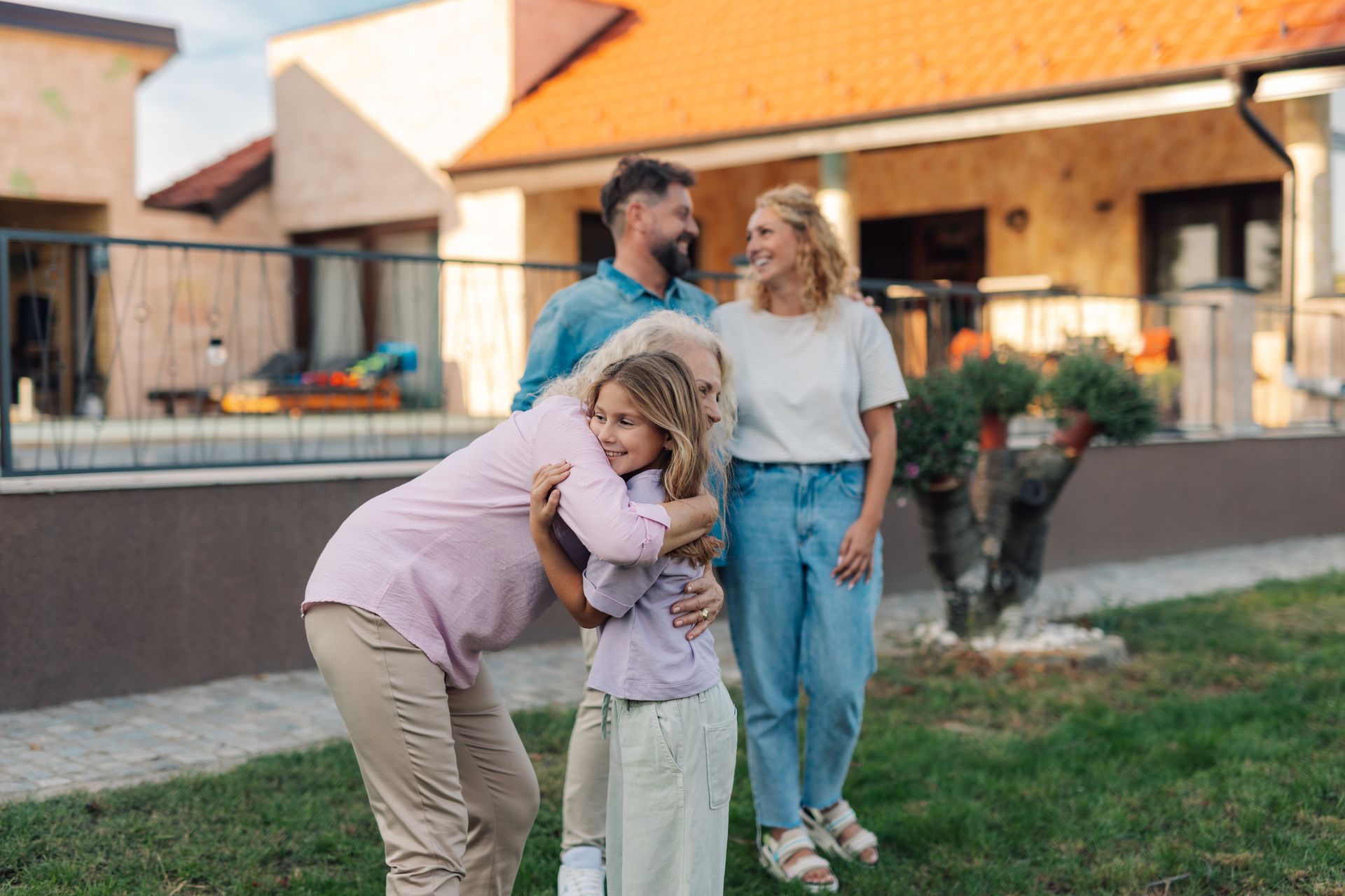 Grandmother hugging granddaughter with family smiling in front of concrete custom home | Nixa, MO