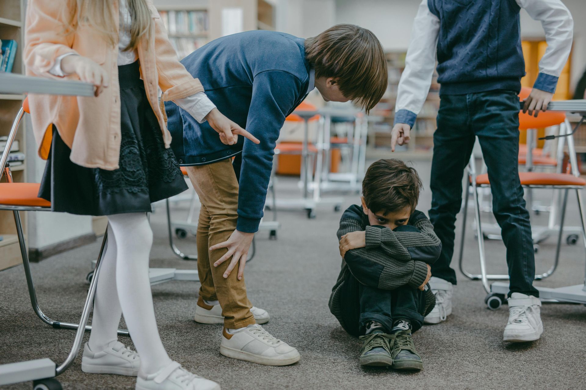Children bullying a student who is sitting on the floor with his head down in a school setting.