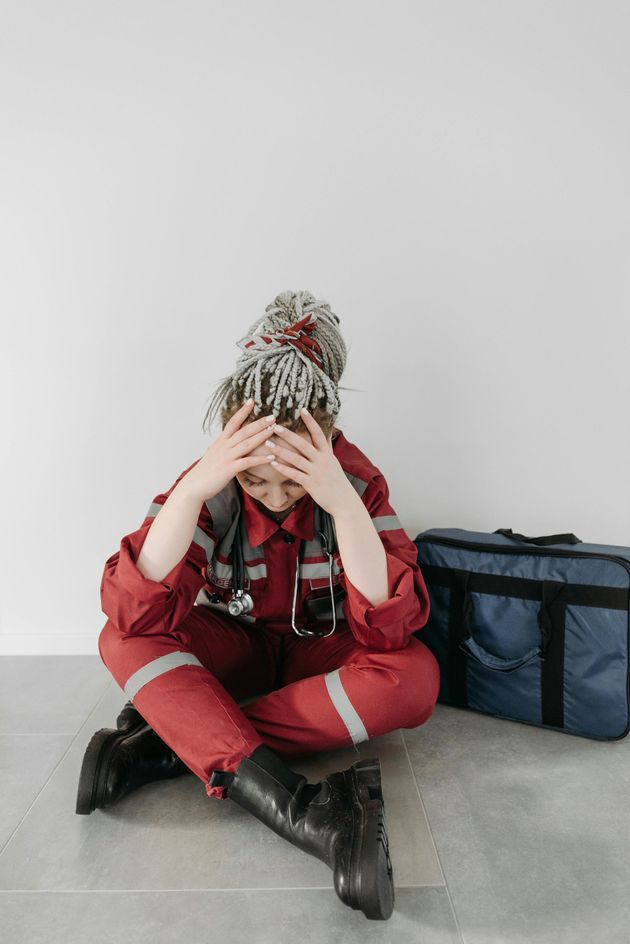 Person in red winter clothes sits on the floor with head in hands beside a blue duffel bag.