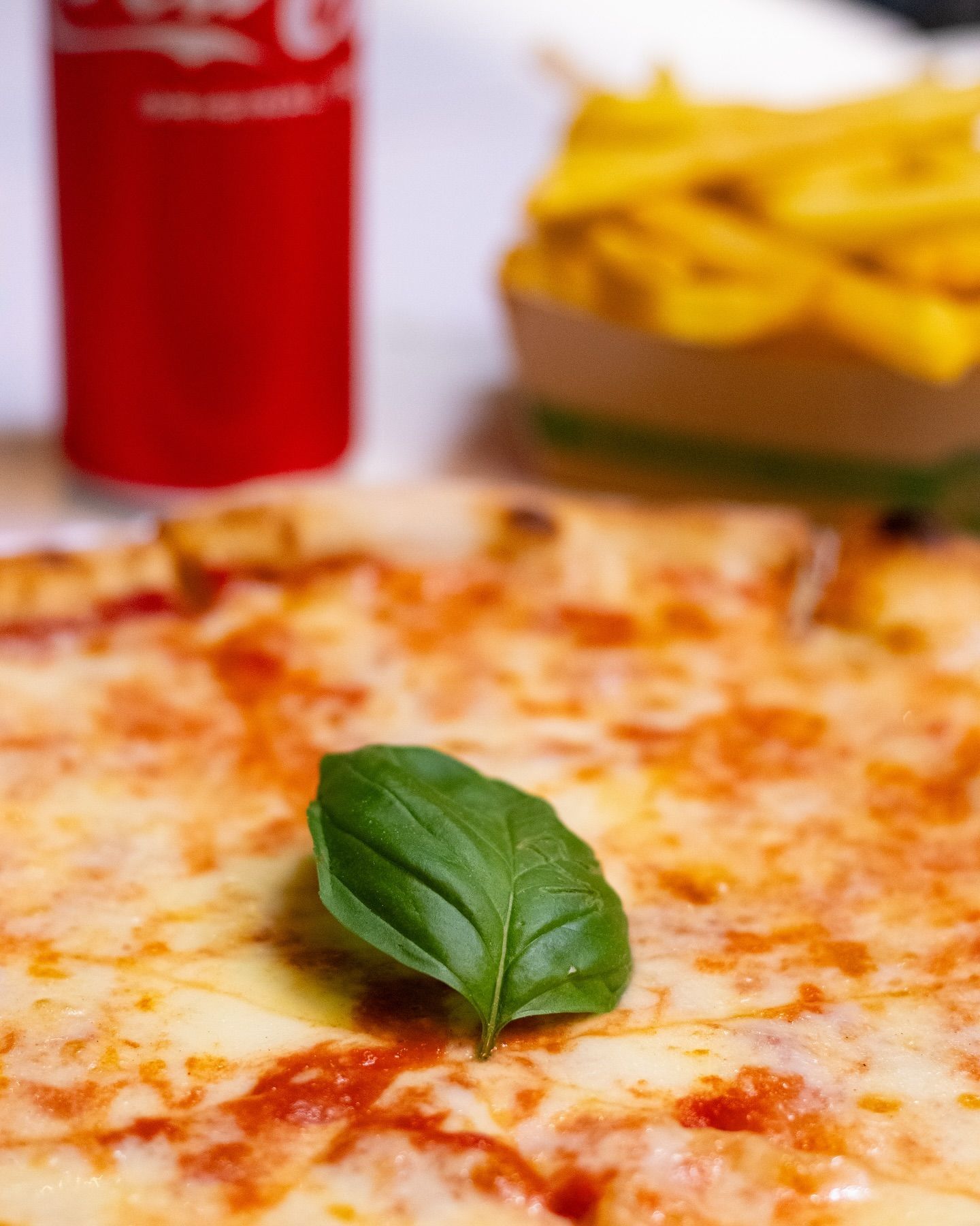Una pizza con una foglia di basilico sopra e una lattina di Coca Cola sullo sfondo.