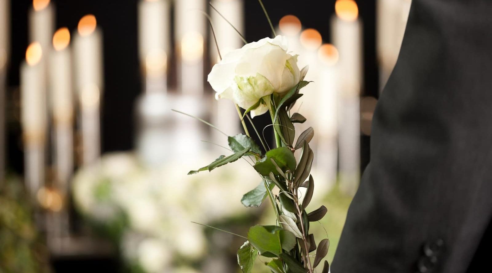 a man in a suit is holding a white rose at a funeral .