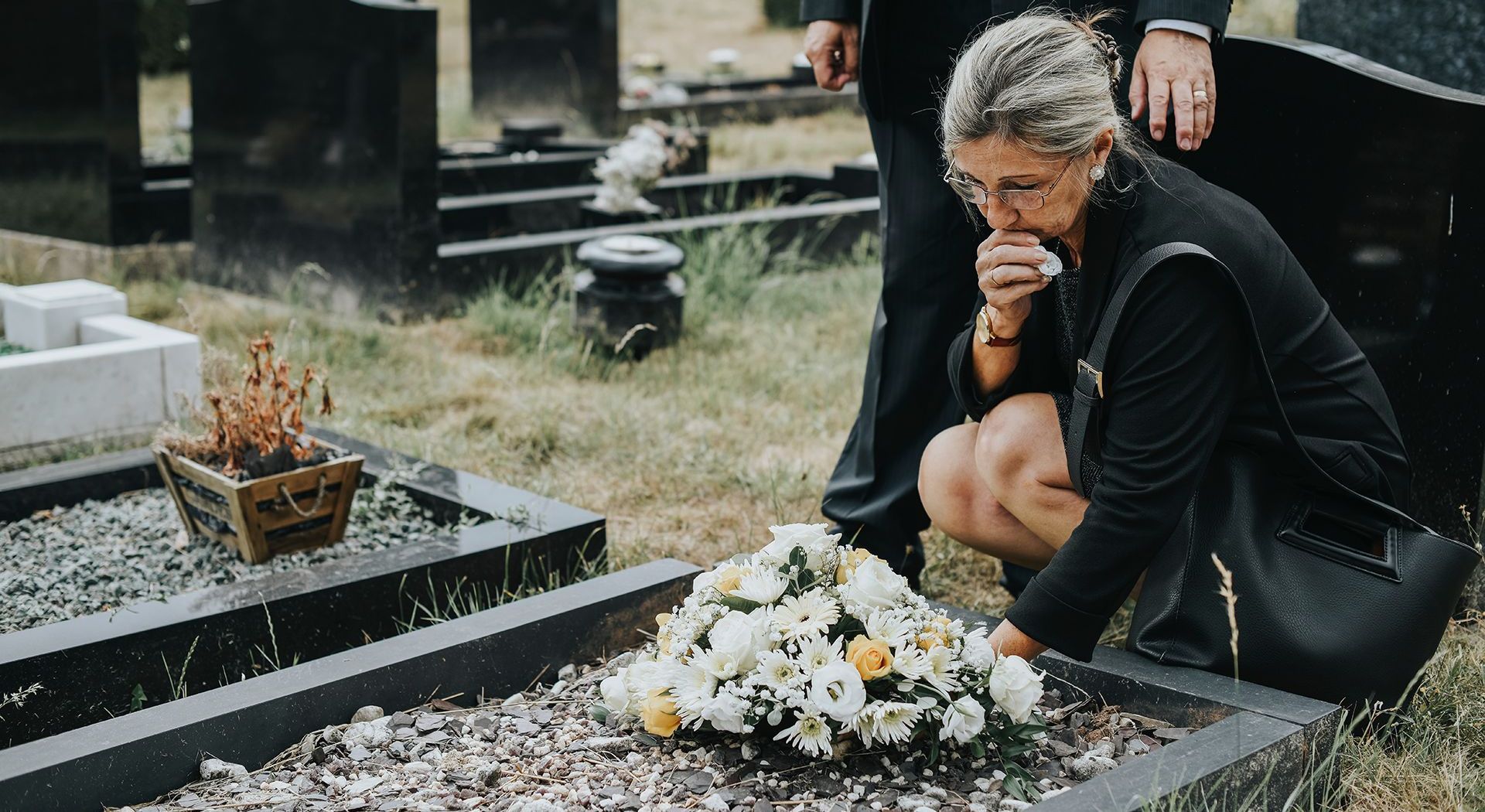 a woman is kneeling down in front of a grave in a cemetery .