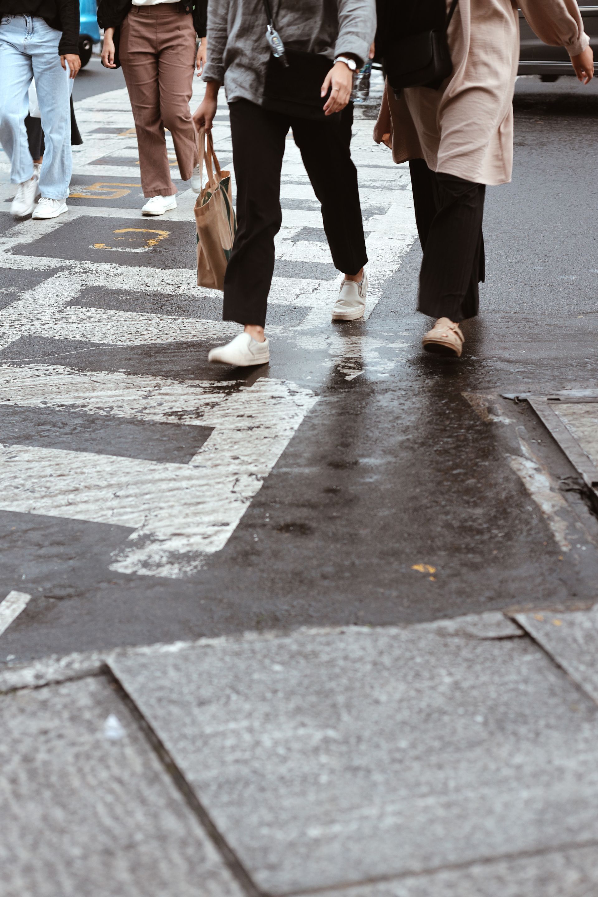 Four people walking across a wet, marked crosswalk on an asphalt city street.