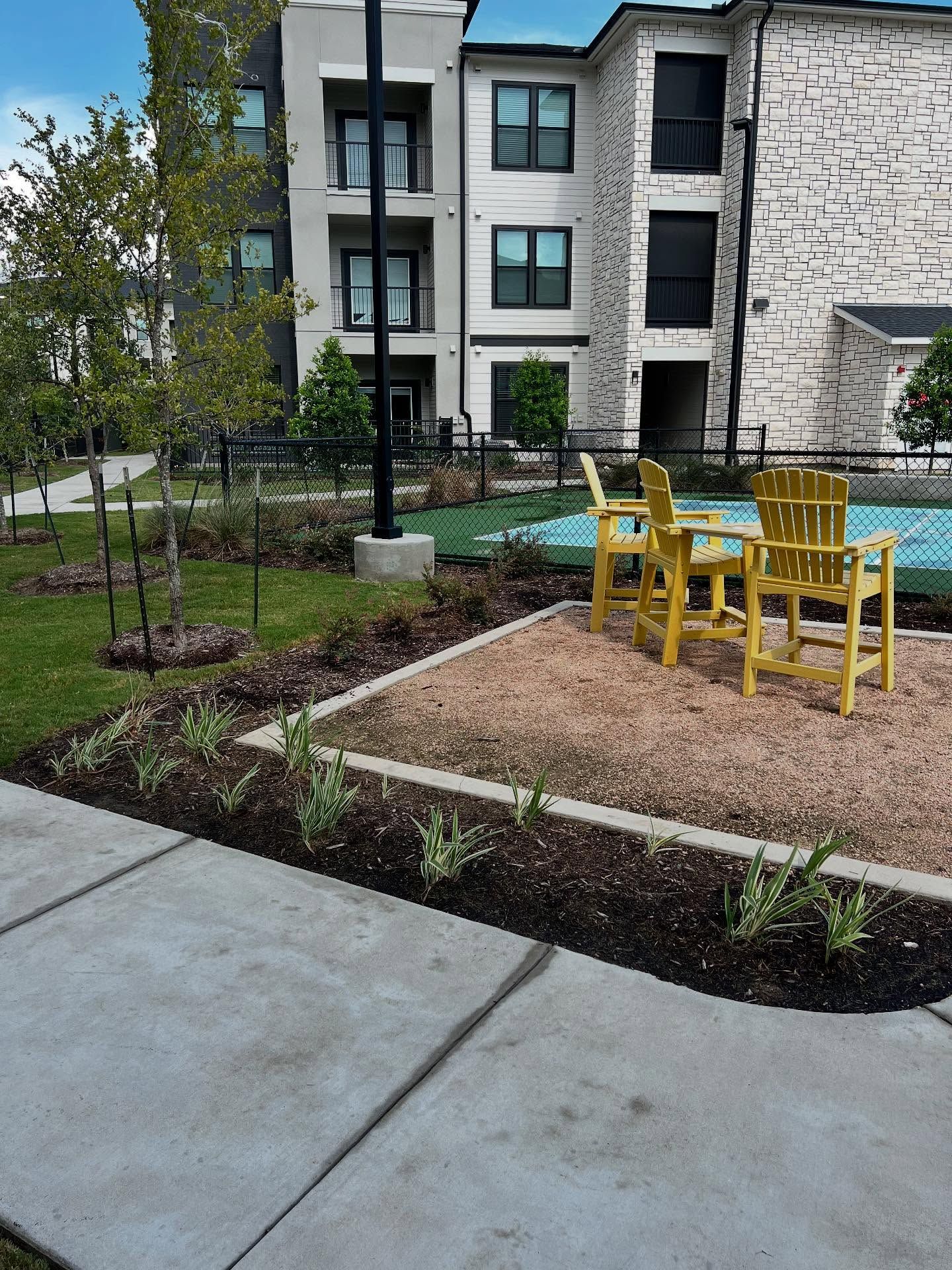 Outdoor seating area with yellow chairs, mulch, landscaping, and apartment building in the background.