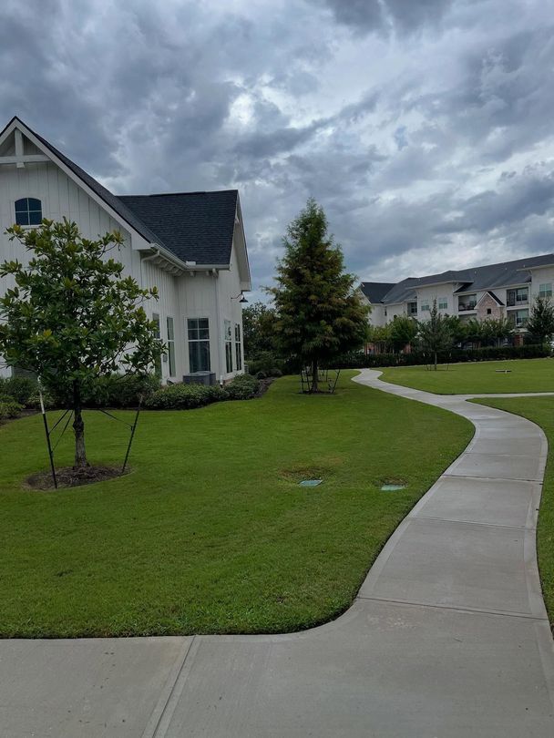 White houses with a curved sidewalk on a green lawn under a cloudy sky.