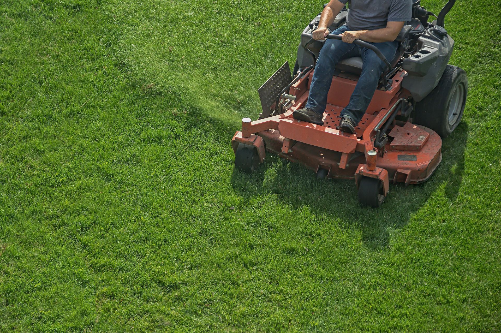 Person on riding lawnmower cutting grass in a green field.