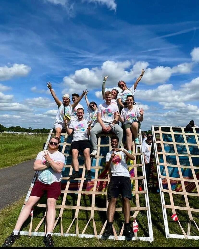 Group of people on an obstacle course, smiling and celebrating against a blue sky.