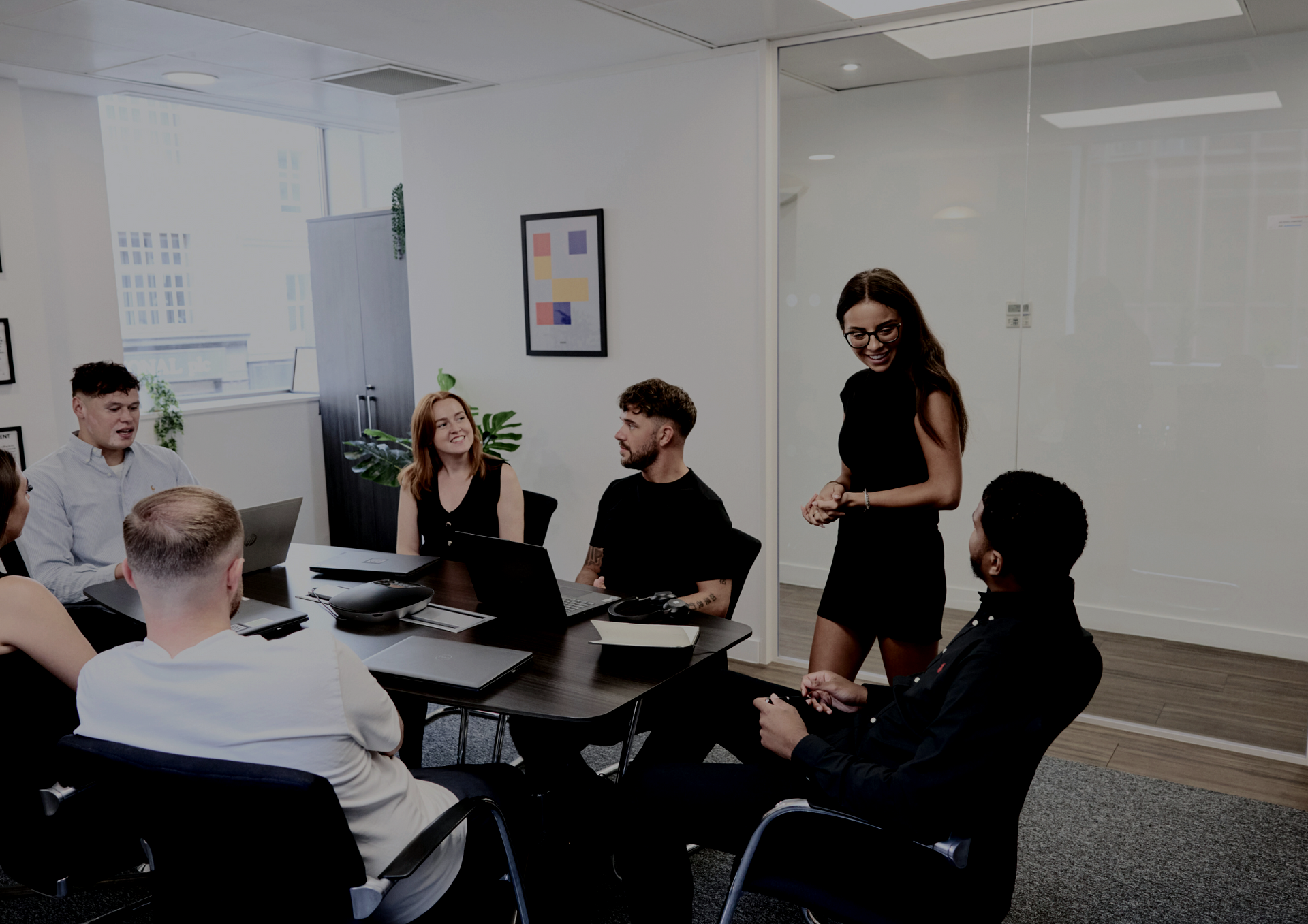Group of people lifting another person, smiling. Neutral background.