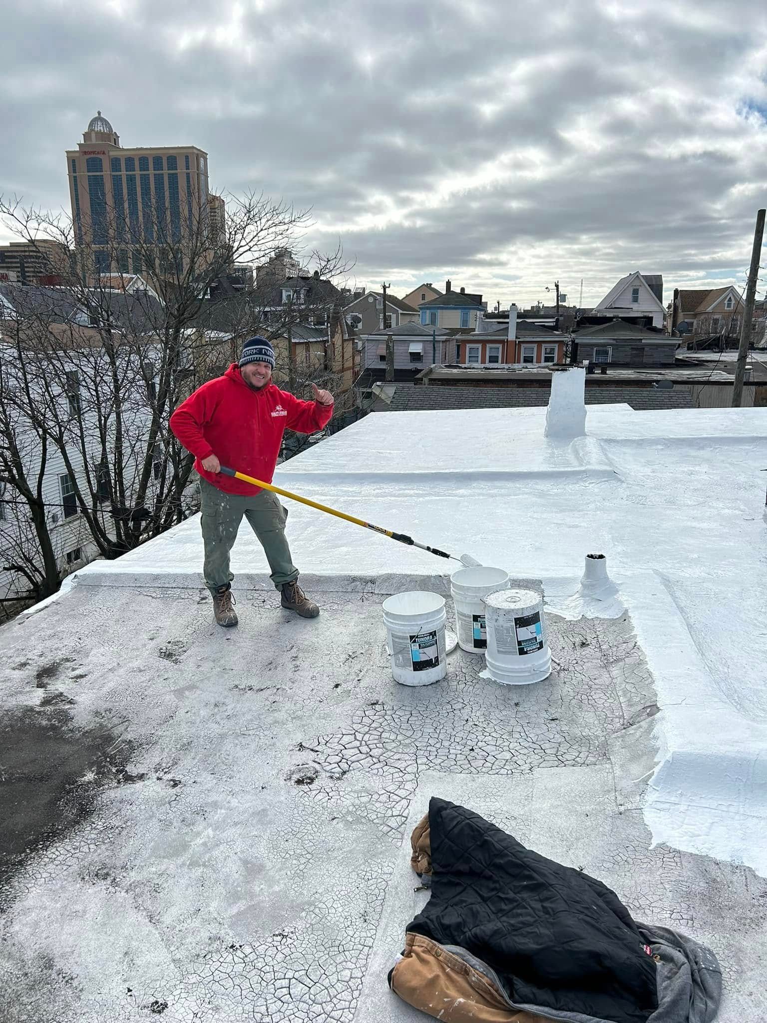 Arturo Ocasio, owner of quality affordable construction llc in red jacket paints a white roof with a roofing sealcoating roller in atlantic city, nj