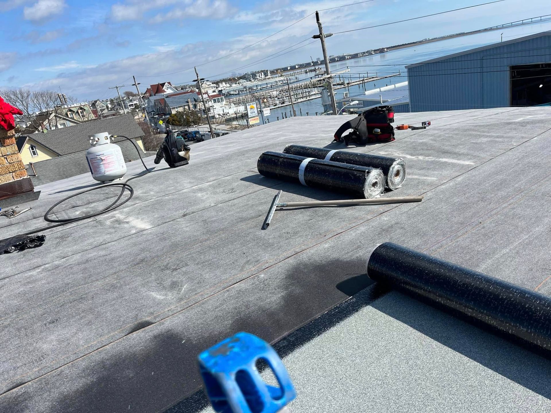 quality affordable construction llc roofers on a flat roof, using propane torch, with rolls of roofing material and view of the bay in atlantic city, nj