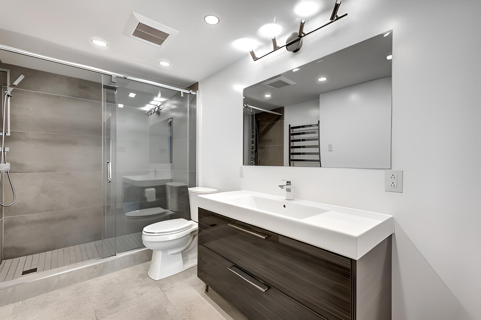 Modern bathroom with gray shower, white toilet, dark vanity, and large mirror installed by quality affordable construction llc