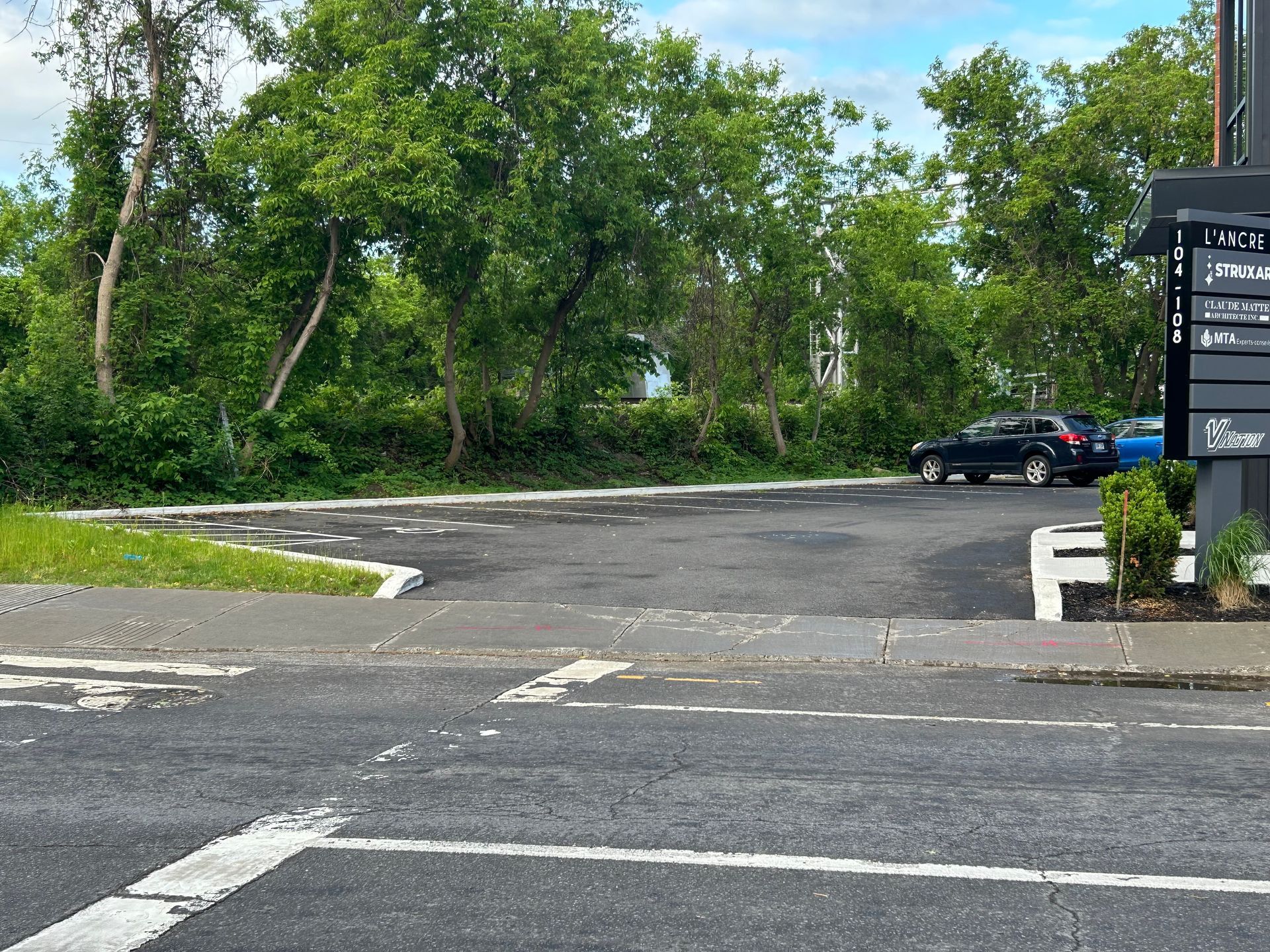 Une voiture est garée dans un parking avec des arbres en arrière-plan.