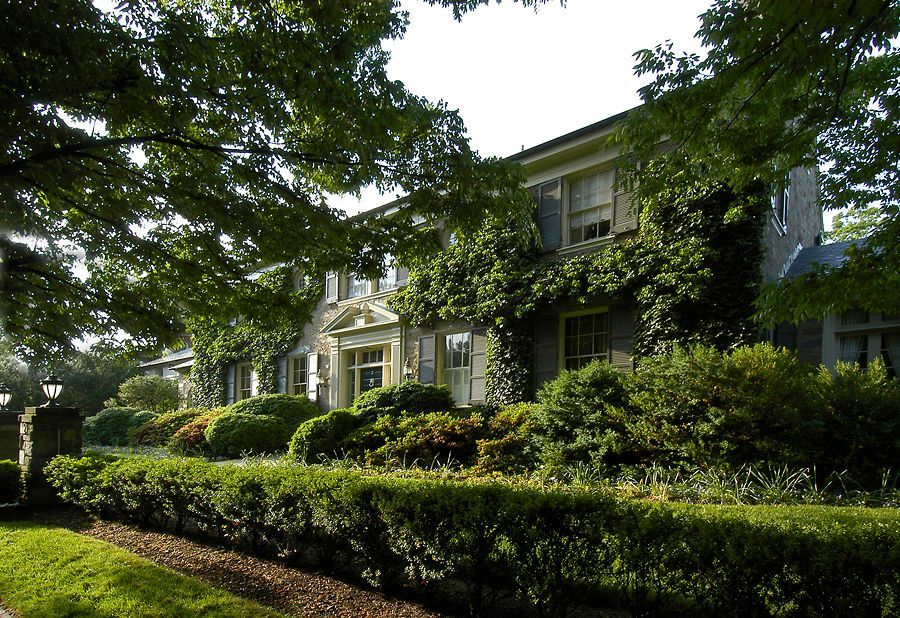 Large stone house with green ivy, trimmed hedges, and leafy trees.