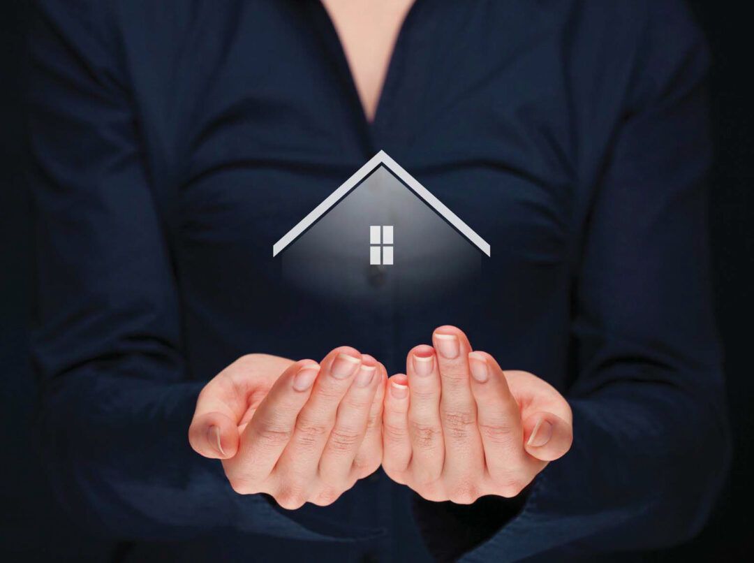 Woman holding a glowing house icon in her cupped hands, symbolizing home ownership.