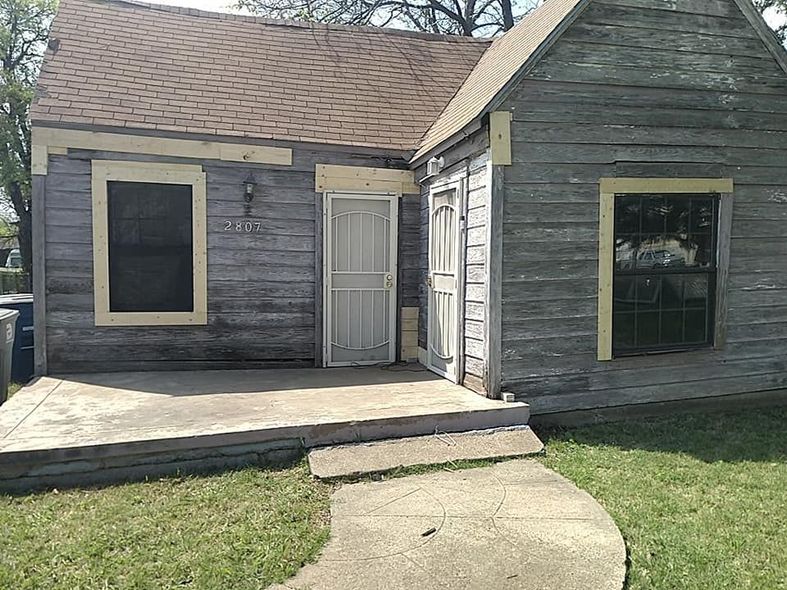 A small wooden house with a concrete walkway leading to it.