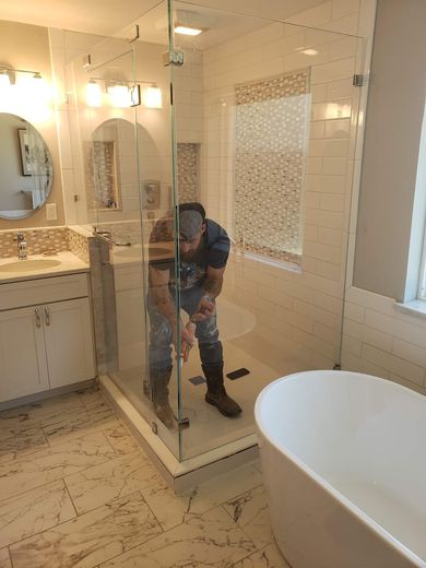 A man is standing in a shower in a bathroom next to a bathtub.