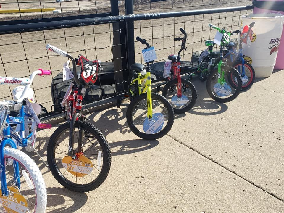 Several children’s bicycles lined up beside a fence on a sidewalk near a road.