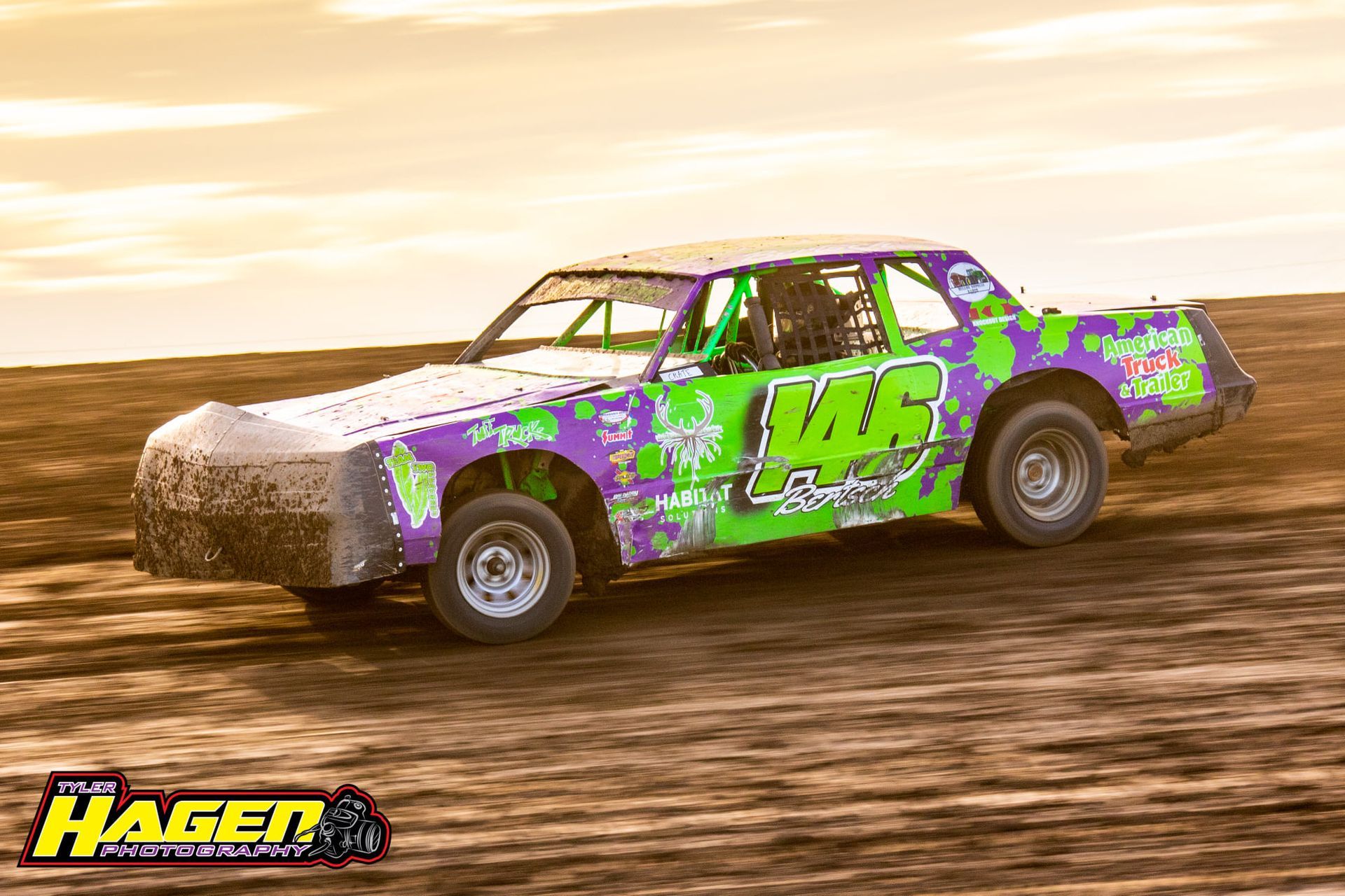 Purple and green dirt track race car kicking up mud on a dirt track at sunset