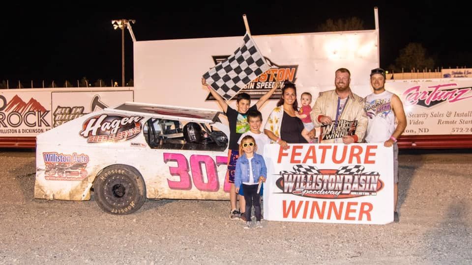 Race car team posing with trophy and “Feature Winner” sign beside a dirt track car at night