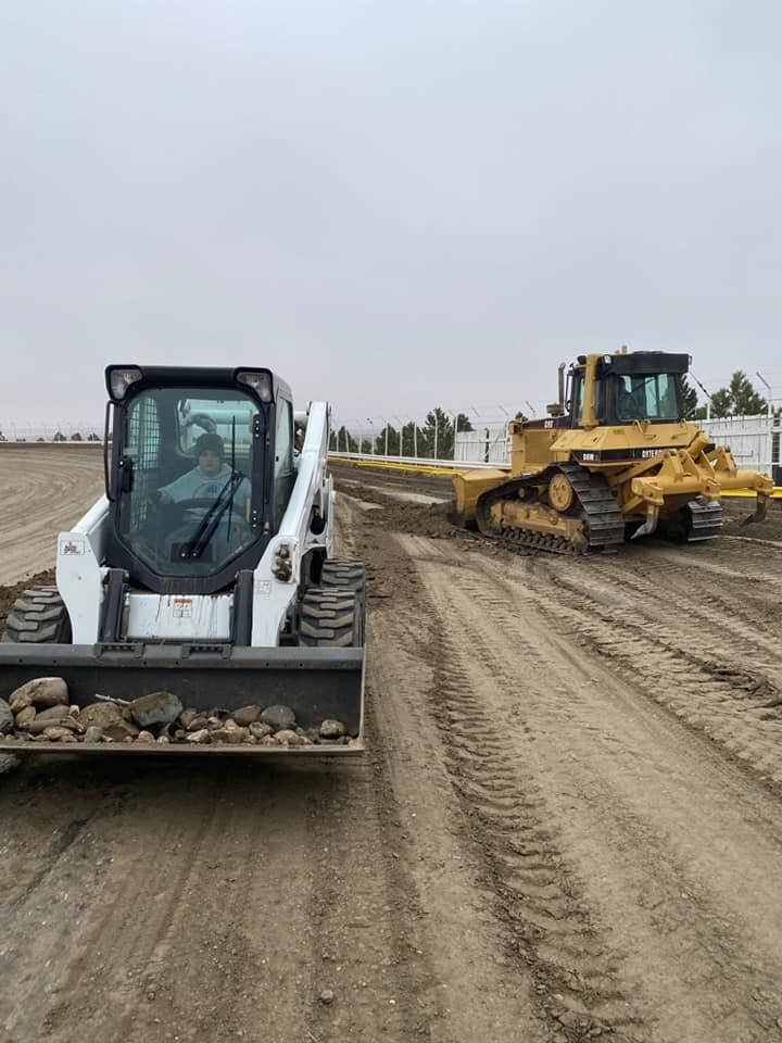 Two construction machines on a dirt road: a white loader in front and a yellow bulldozer behind.