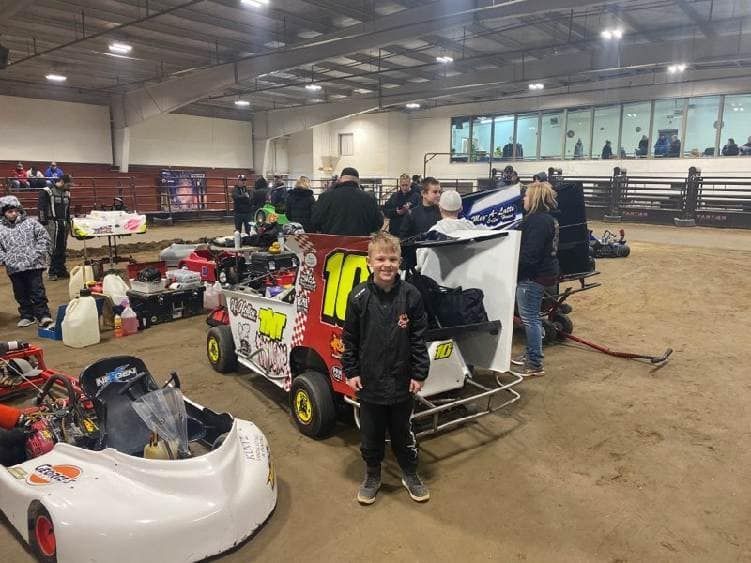 Indoor go-kart pit area with riders and carts, including a red and yellow kart in the foreground.