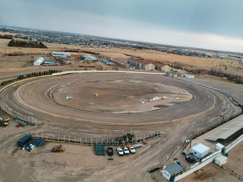 Aerial view of a large circular dirt racetrack with vehicles and equipment around it in a rural landscape
