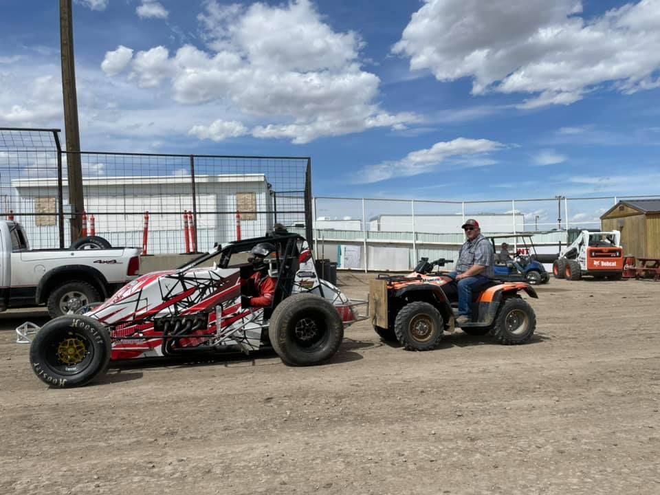 Two off-road vehicles parked on a dirt lot under a cloudy blue sky.