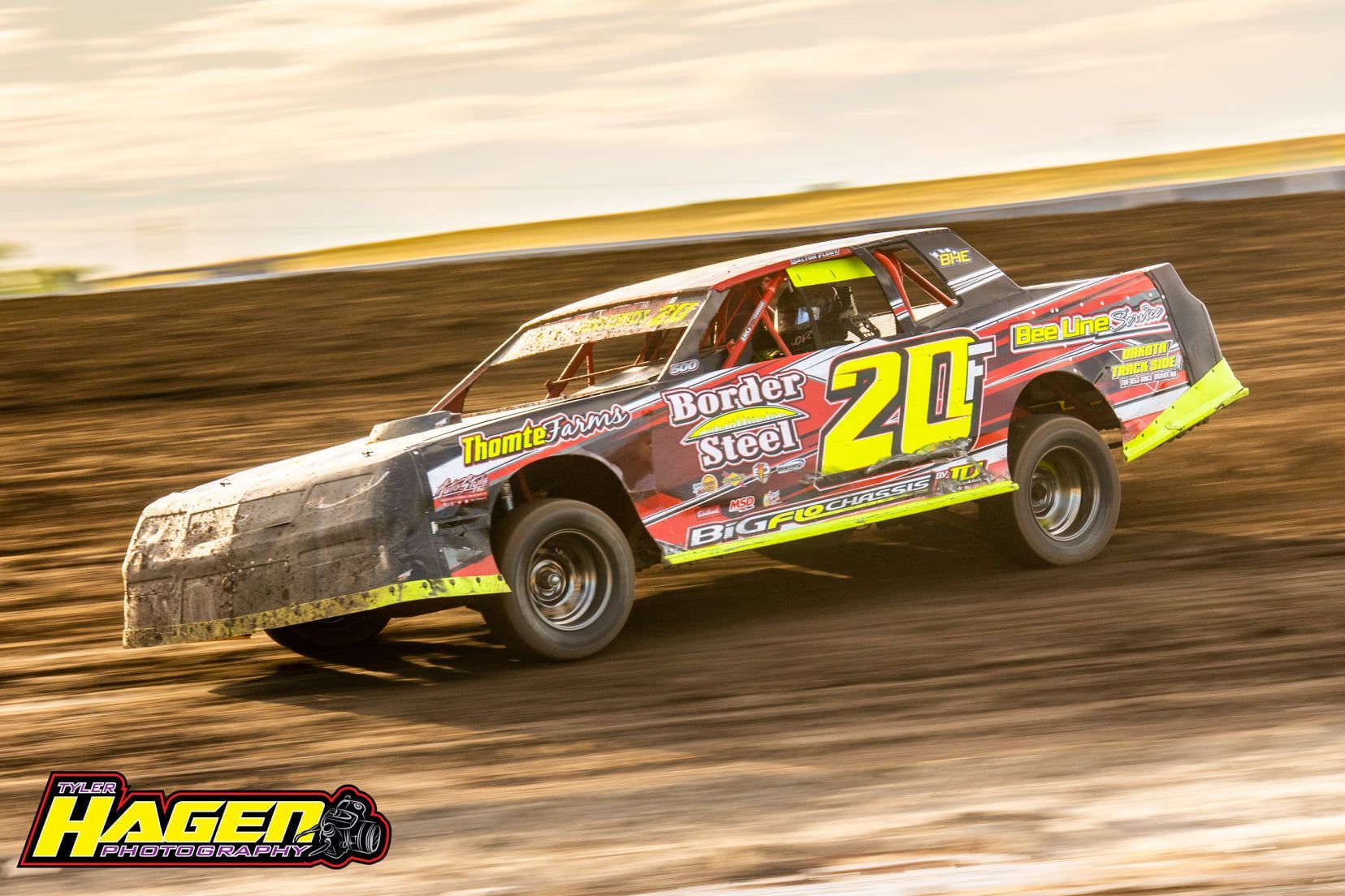 Yellow No. 20 dirt track race car speeding on a muddy oval track at sunset
