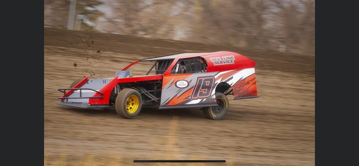 Red and silver dirt track race car speeding through a muddy turn on a dirt oval track.