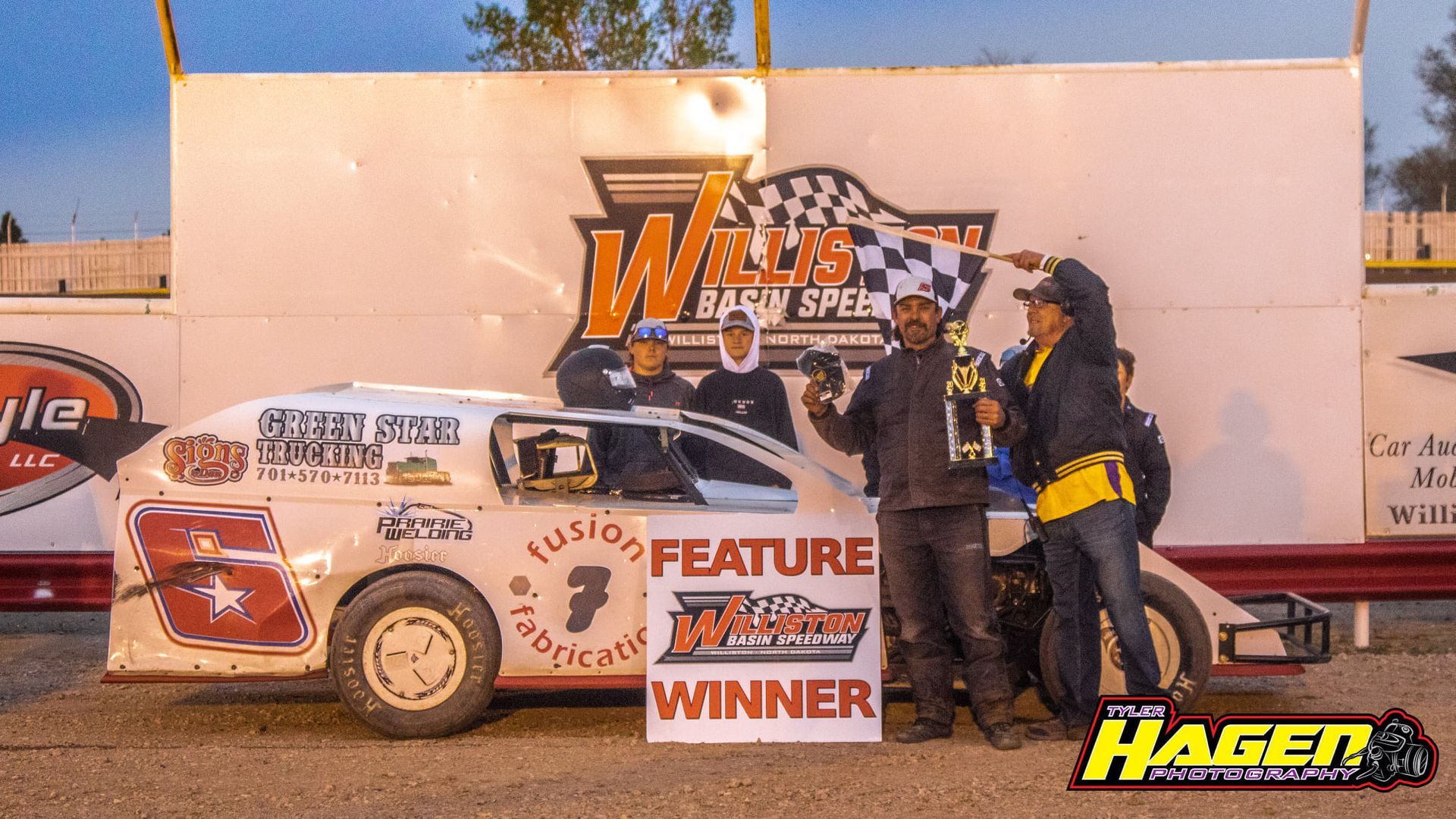 Racing car winner celebration with two people and a trophy in front of a sponsor backdrop