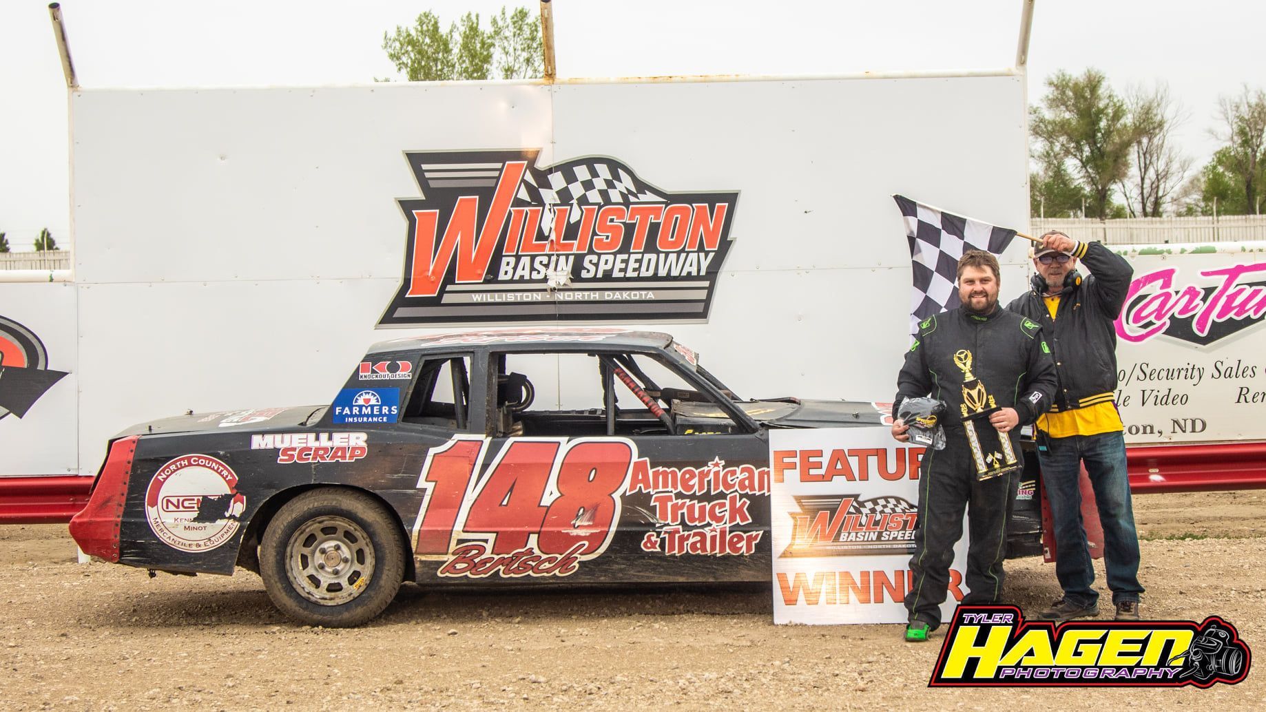 Race car with driver holding a checkered flag beside a trophy, sponsored by Walters Fast Service and Hagen.