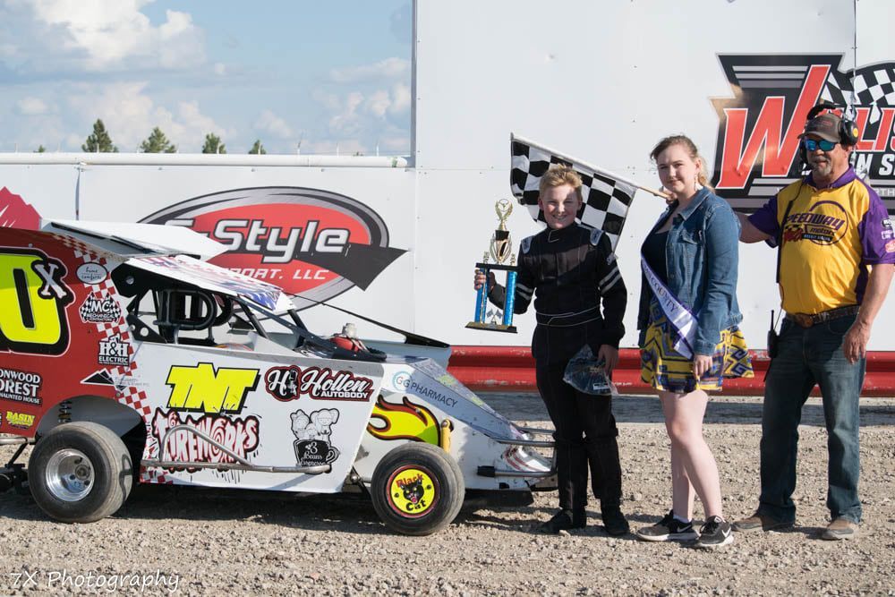Three people standing beside a colorful race car with sponsor decals at a dirt track.