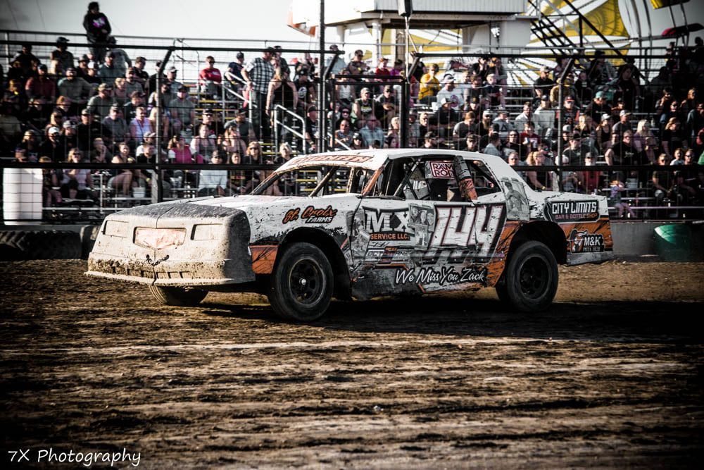 Red and white stock car racing on a dirt track before a packed grandstand