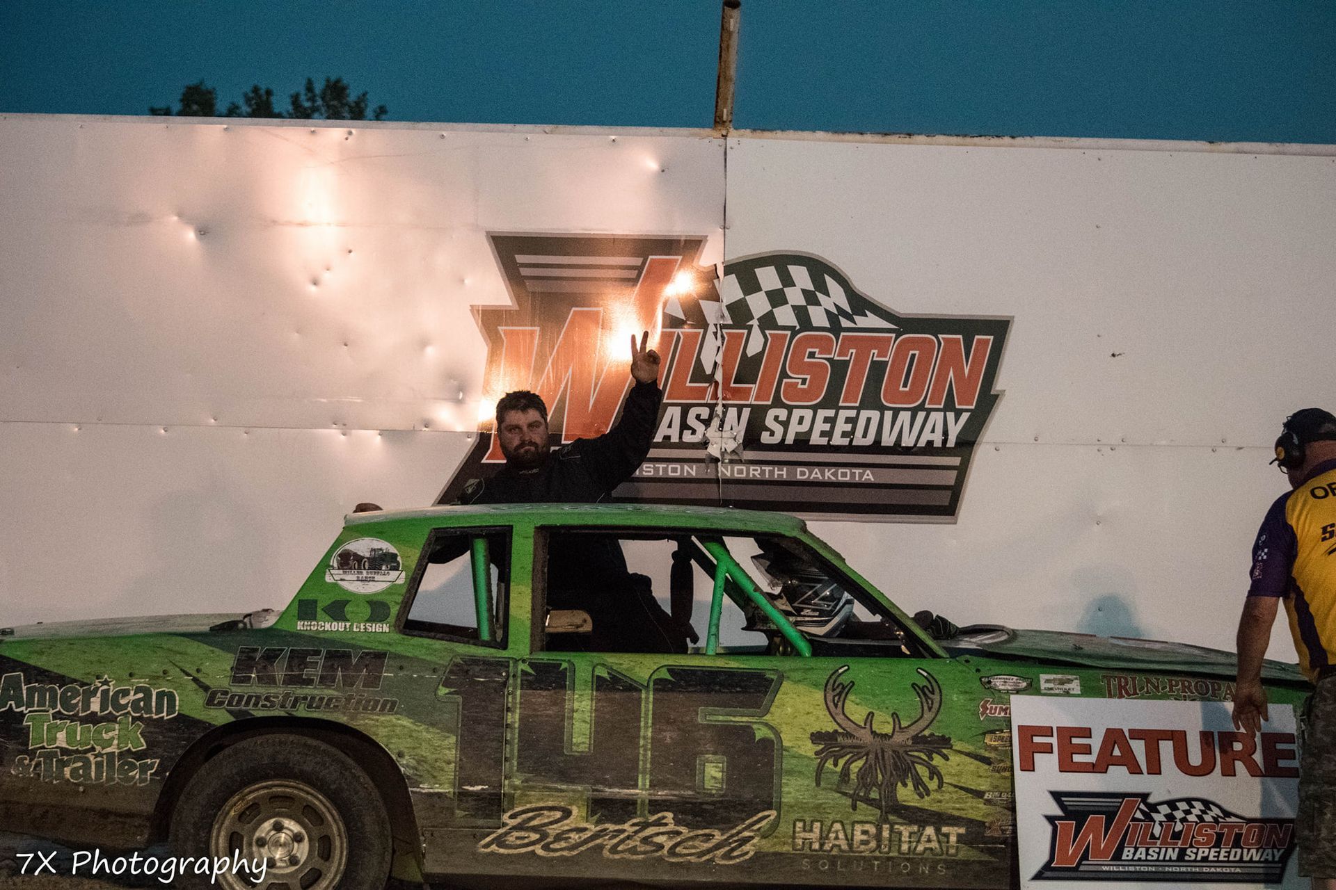 Green dirt track race car with driver celebrating at the finish line under the Elliston Speedway sign
