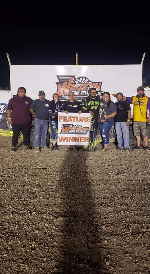 Group of people posing at night beside a “Feature Winner” sign on a dirt track.