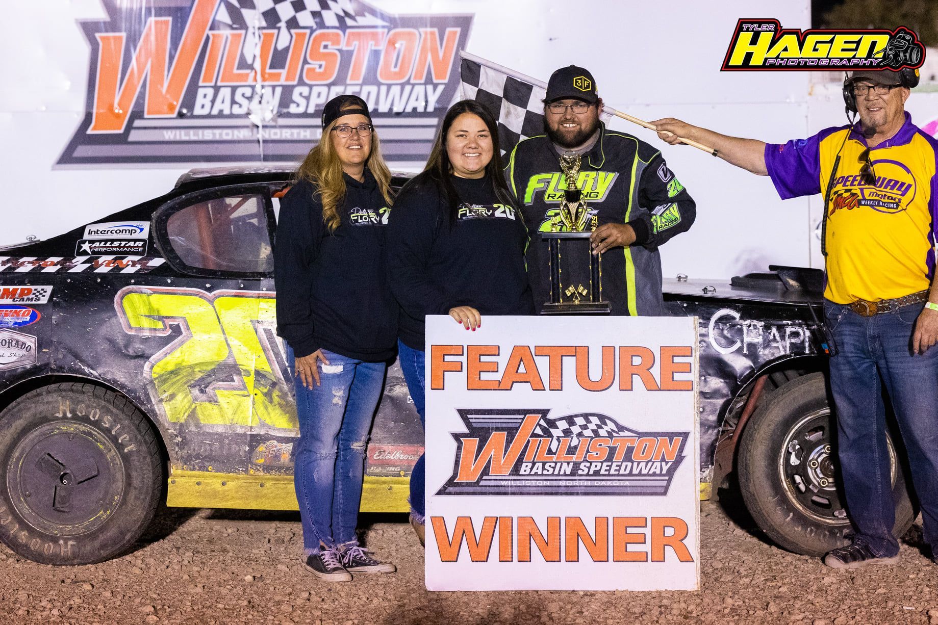 Race winners posing with a feature winner sign in front of a dirt track car at Williston Basin Speedway
