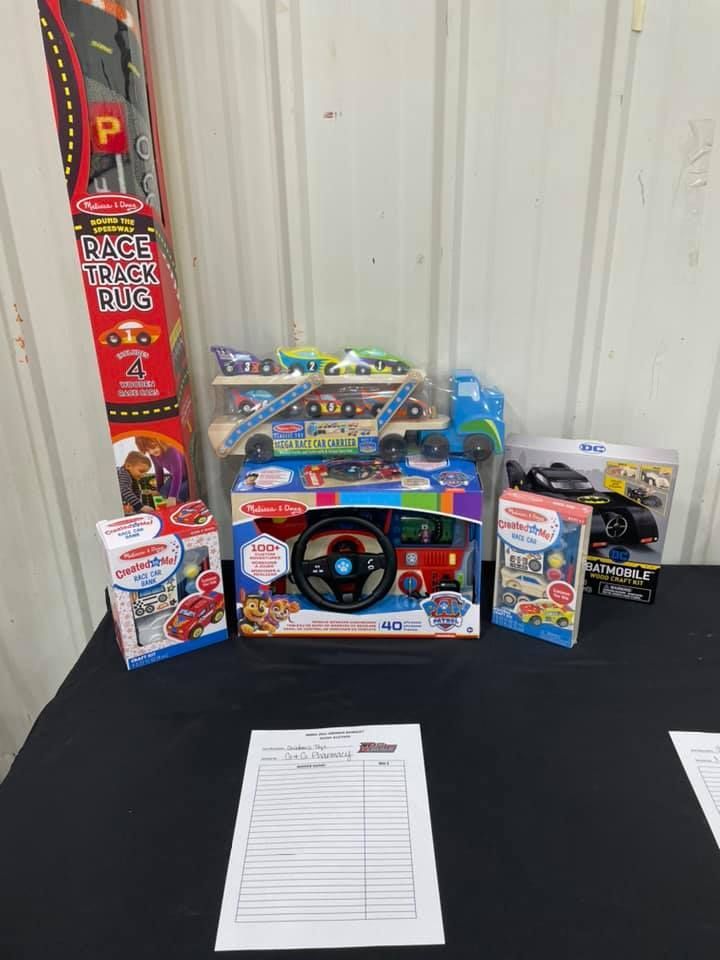Assorted toys displayed on a black table with a raffle ticket sheet in front, against a metal wall.