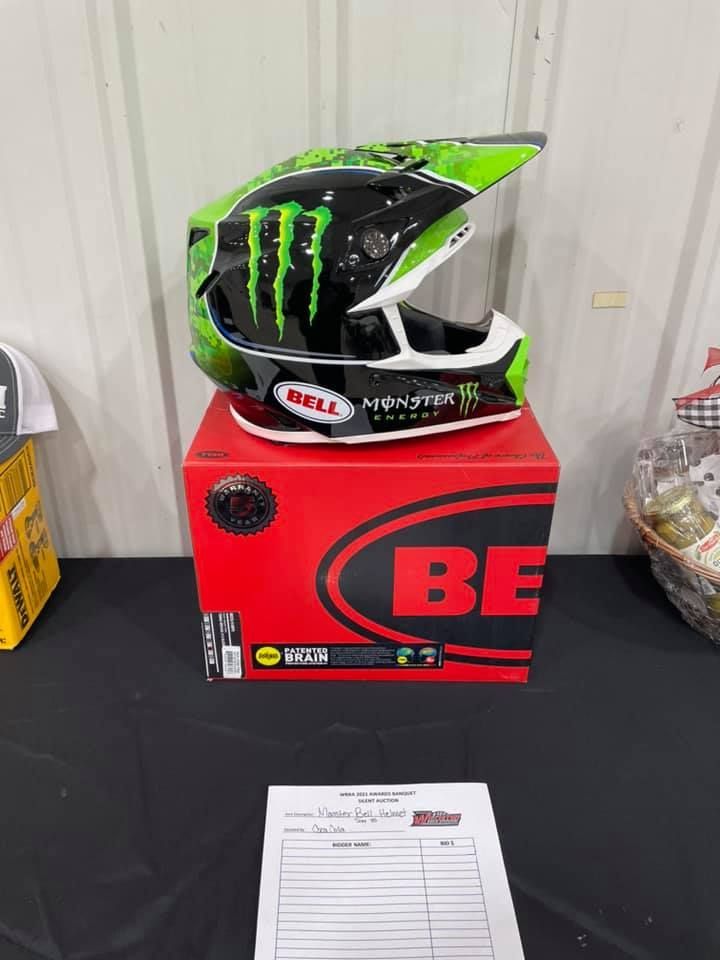 Green Monster Energy motocross helmet on a red Bell box, displayed indoors on a table.