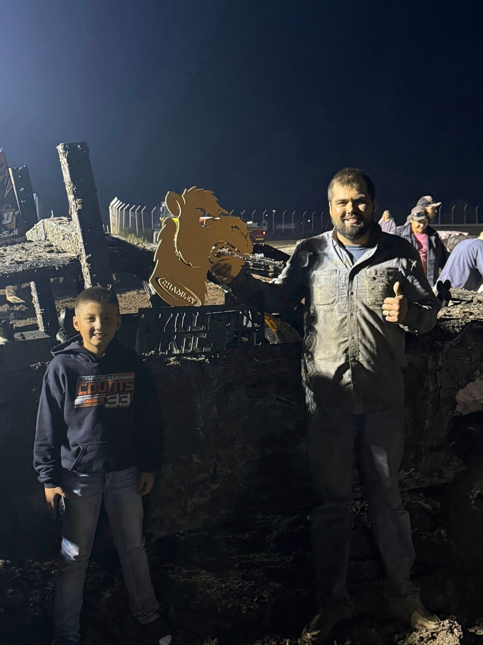 Two people posing at night beside a city skyline, holding a gold puzzle-piece-shaped trophy.