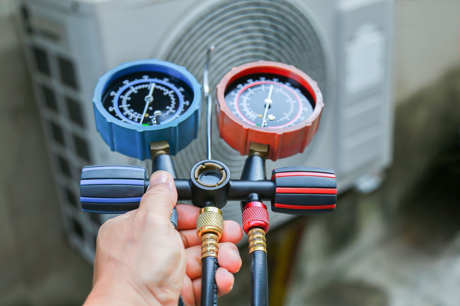 A person is holding a pressure gauge in front of an air conditioner.