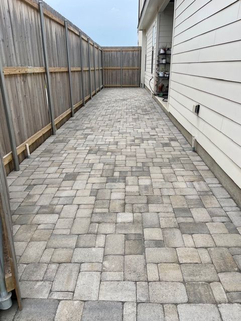 Brick paved walkway between wooden fence and house.