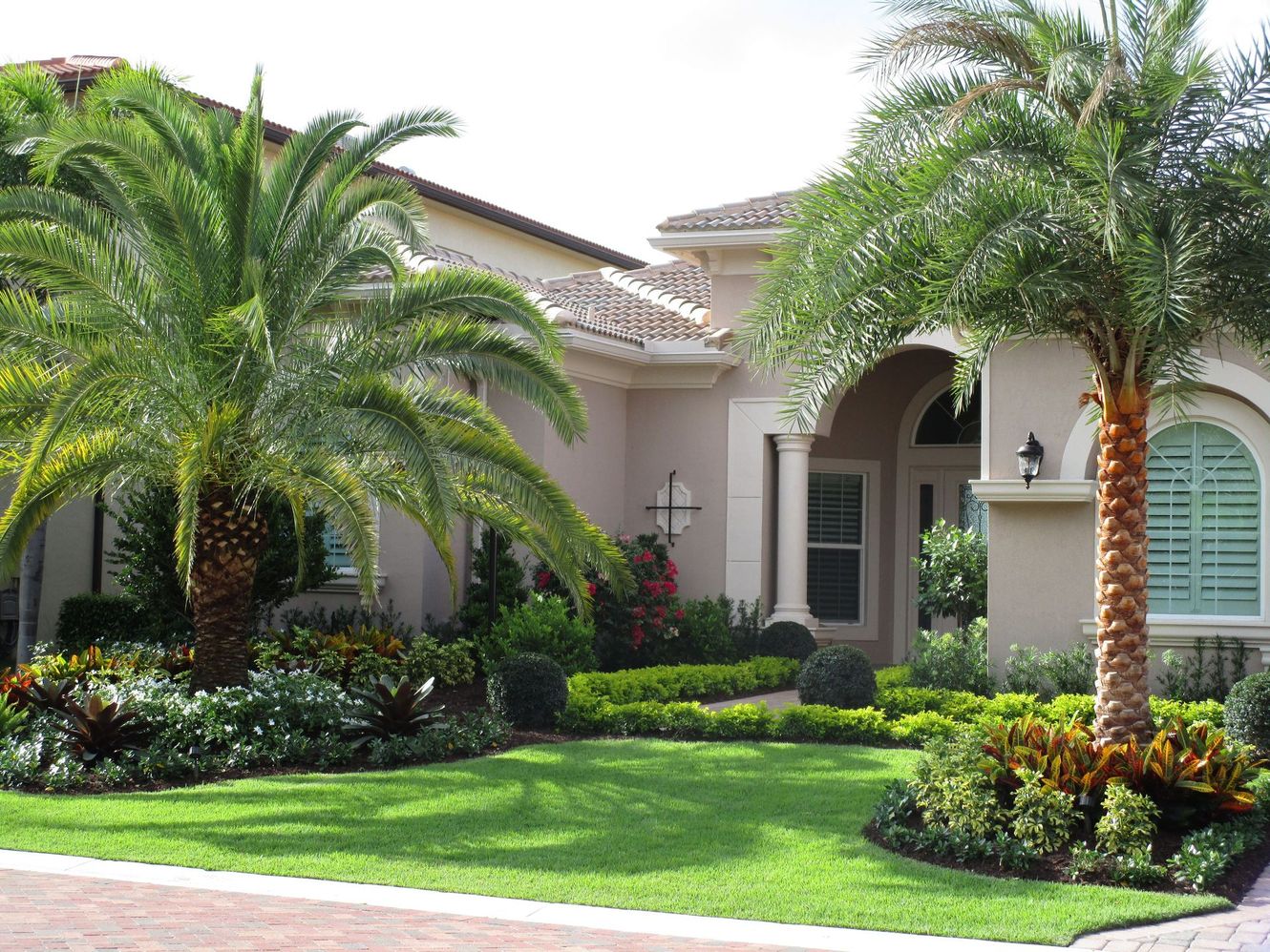 Beau Monde Landscaped a house with a manicured lawn, palm trees, and flowering landscaping